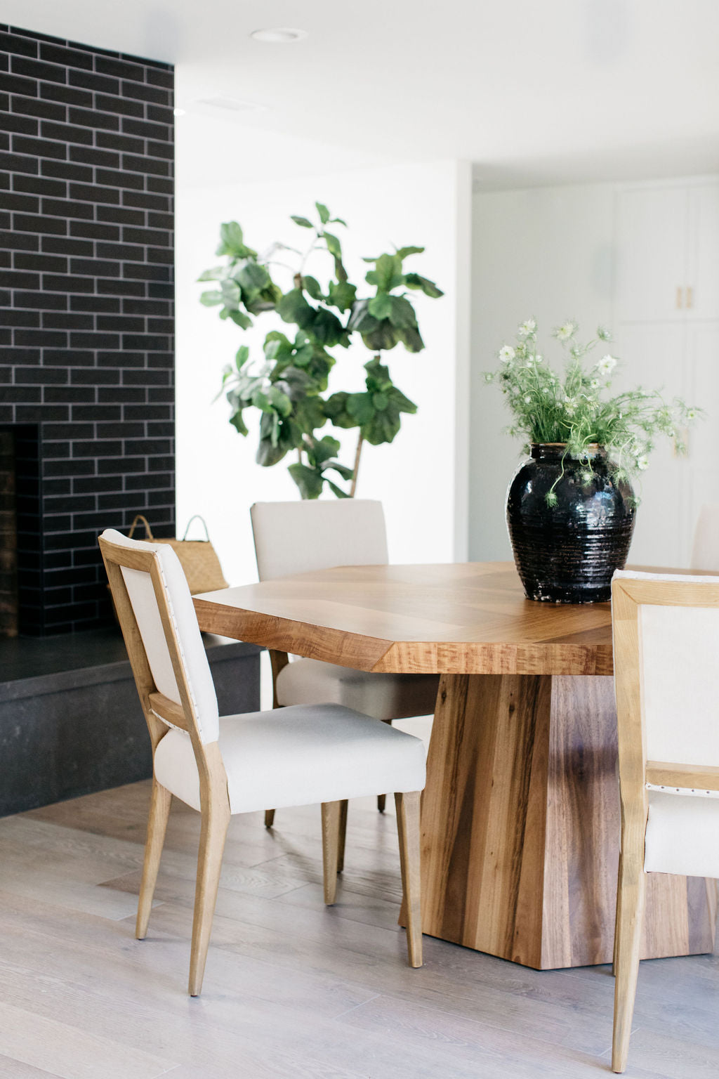 greige design shop + interiors asymetrical dining table and white upholstered dining chairs black tile fireplace